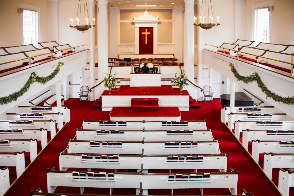 Empty wooden pews and plain windows inside the church, looking towards the front